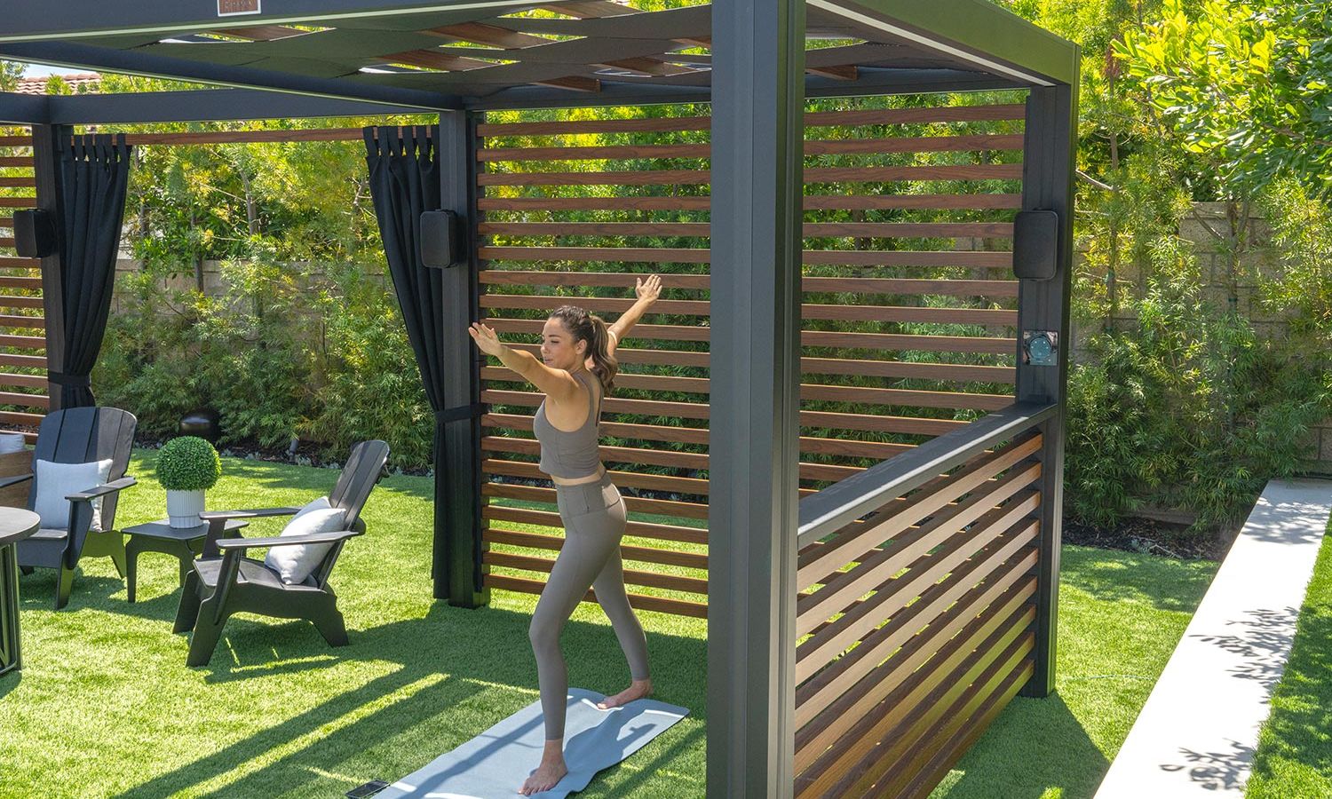 A group of friends relaxes in a hot tub at night, watching a large outdoor screen displaying an underwater scene. The cozy backyard setting is illuminated by ambient lighting and a fire bowl.